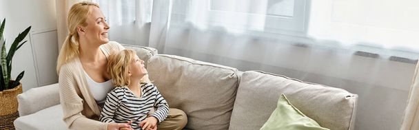 χαρούμενη μητέρα αγκαλιά κόρη σε casual ενδυμασία και κάθεται μαζί στον καναπέ στο σαλόνι, πανό - Φωτογραφία, εικόνα