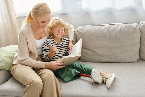 μητέρα διαβάζει βιβλίο στην ευτυχισμένη κόρη της με προσθετικό πόδι και κάθεται μαζί στο σαλόνι - Φωτογραφία, εικόνα