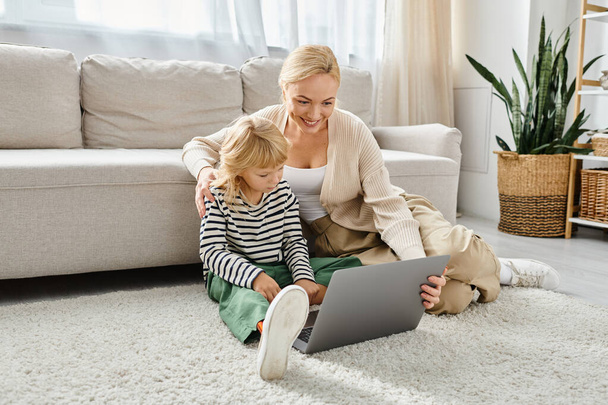 χαρούμενο παιδί με προσθετικό πόδι που χρησιμοποιεί φορητό υπολογιστή και κάθεται στο χαλί με τη μητέρα στο σαλόνι - Φωτογραφία, εικόνα