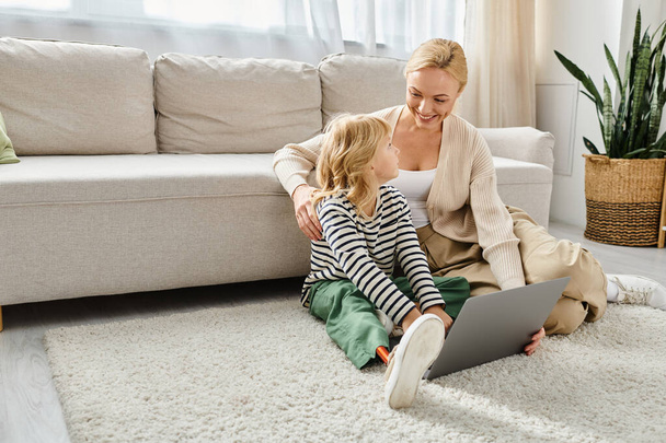 gelukkig kind met prothese been met behulp van laptop en zitten op tapijt met moeder in de woonkamer - Foto, afbeelding