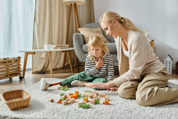 Девушка-инвалид с протезной ногой сидит на ковре и смотрит на деревянные игрушки рядом с матерью - Фото, изображение