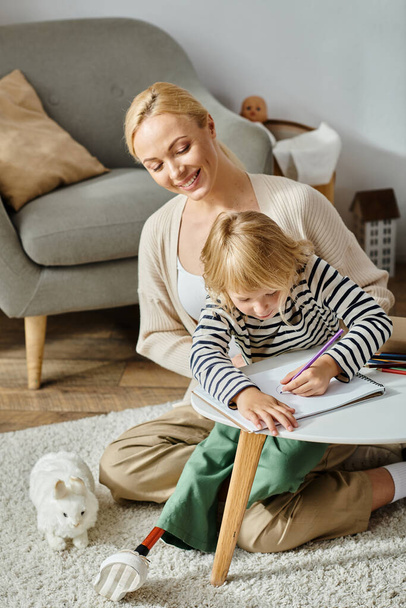 блондинка с протезом ноги рисунок на бумаге с красочными карандашами возле счастливой матери дома - Фото, изображение