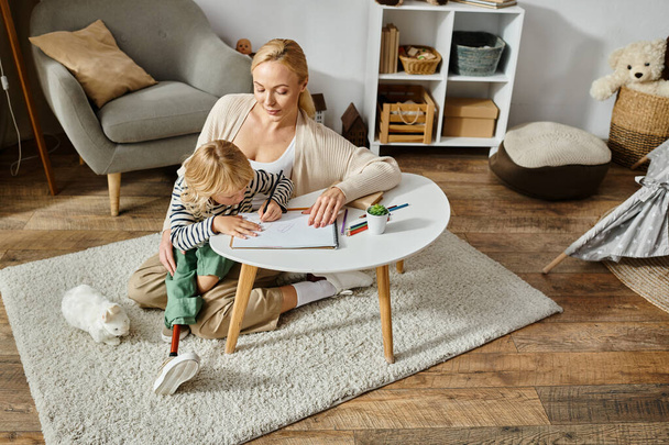 ευτυχισμένη γυναίκα κοιτάζοντας την κόρη με προσθετικό πόδι σχέδιο σε χαρτί με πολύχρωμο μολύβι, γενικά - Φωτογραφία, εικόνα