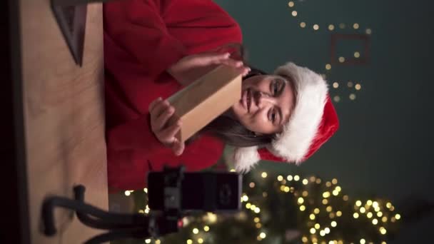 Nuori vaikuttaja unboxing tech tuote ja ammunta video sosiaalisen median istuu kotona jouluna. Pystysuora video - Materiaali, video