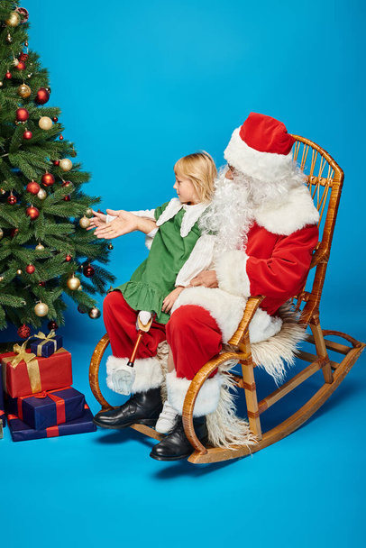 szczęśliwa dziewczyna z protezą nogi siedzi na kolanach Świętego Mikołaja obok ozdobionej choinki - Zdjęcie, obraz