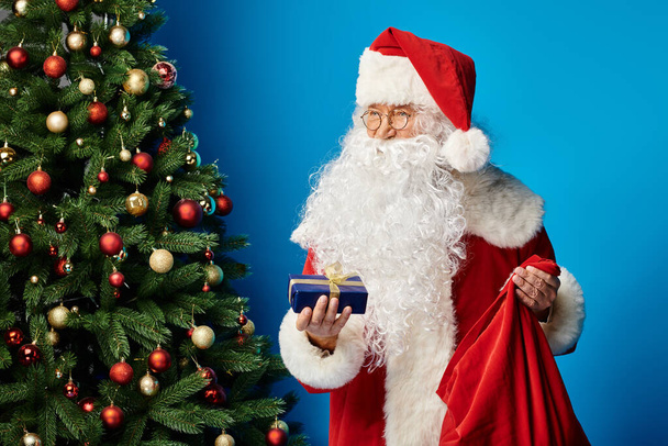glücklicher Weihnachtsmann mit Bart und Brille im roten Kostüm mit Sacksack und Weihnachtsgeschenk - Foto, Bild