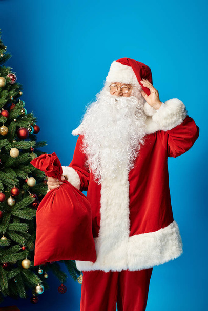 gelukkig kerstman met baard en bril in rood kostuum holding zak zak met kerstcadeaus - Foto, afbeelding