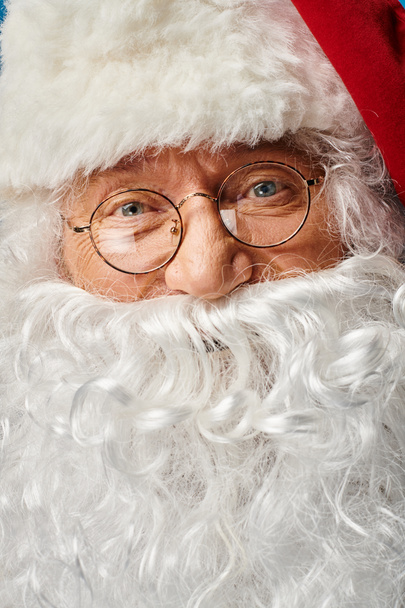 close-up van gelukkig kerstman met witte baard en bril kijken naar camera op blauwe achtergrond - Foto, afbeelding