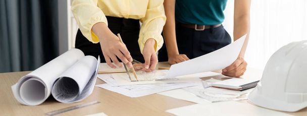 Professional architect team used divider measure during draft blueprint on table with architectural document, safety helmet and blueprint scatter around. Closeup. Focus on hand. Delineation. - Photo, Image