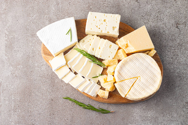 Ξύλινη σανίδα με διάφορα τυριά και ελιές. Μπρι. Καμεμπέρ. Παρμεζάνα, φέτα, μπλε τυρί. Ιταλικό, γαλλικό τυρί. - Φωτογραφία, εικόνα