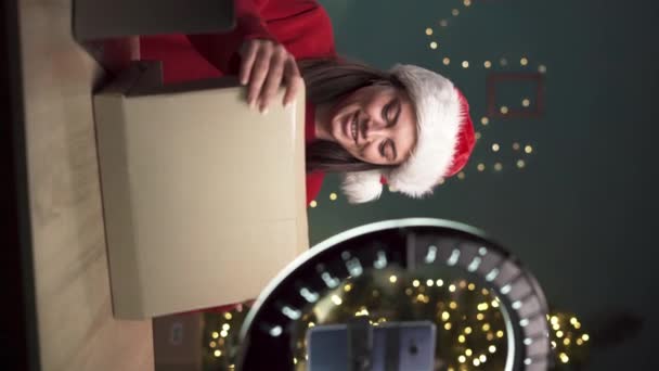 Female blogger unpacking gift box present from companies on Christmas and doing livestreaming. Woman using camera for creating content. Vertical video - Footage, Video