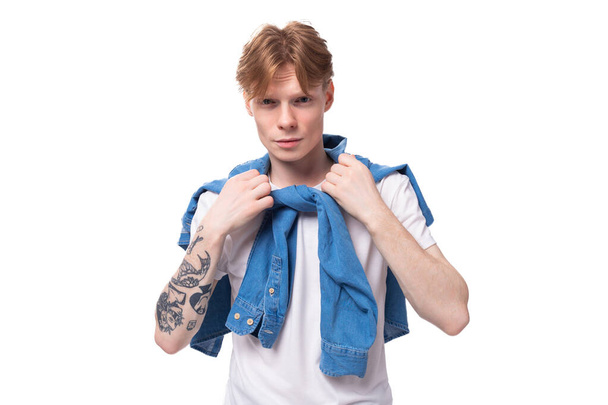 joven pelirrojo chico con un peinado fresco se viste con una camisa de mezclilla azul sobre un fondo blanco. - Foto, imagen