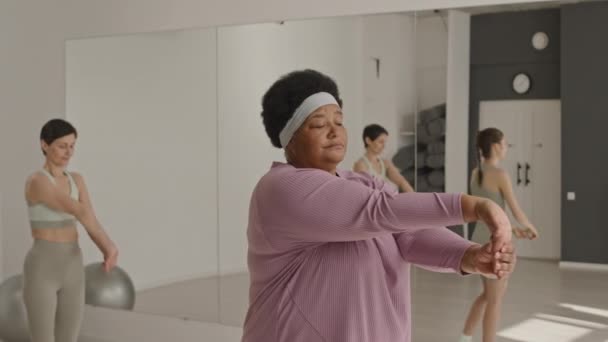 Medium shot van volwassen zwarte vrouw in sportkleding doen pols stretch met behulp van jonge vrouwelijke fitness instructeur tijdens groepstraining - Video