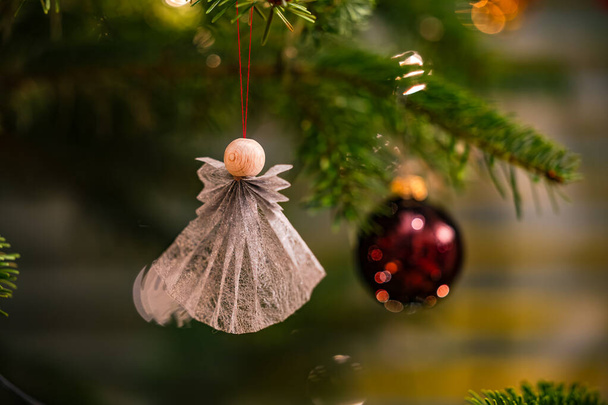 Een zelfgemaakte engel en een rode kerstboom bal op de sparren takken van de kerstboom met Kerstmis - Foto, afbeelding