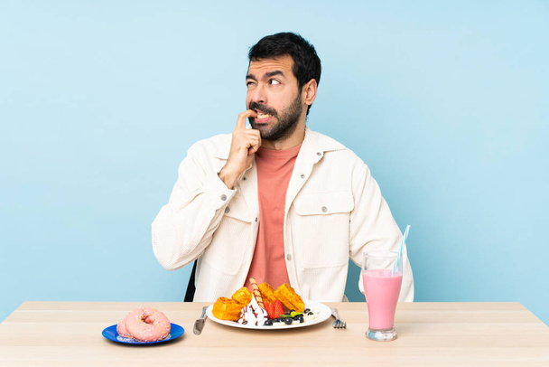 Hombre en una mesa desayunando gofres y un batido nervioso y asustado - Foto, Imagen
