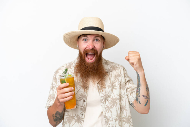 Kızıl saçlı, uzun sakallı, kumsalda kokteyl içen, beyaz arka planda izole bir adam zaferi kutluyor. - Fotoğraf, Görsel