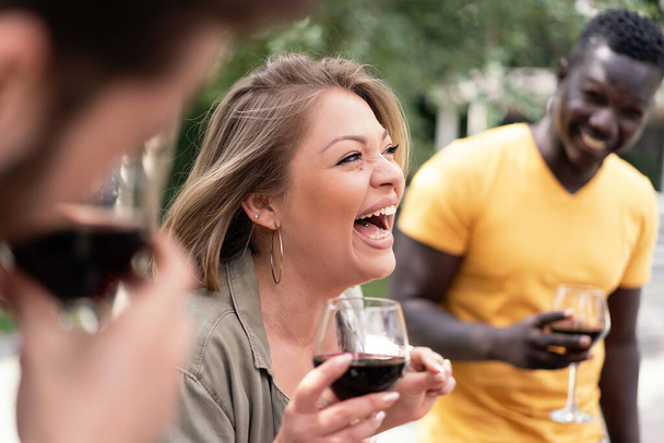 Le rire contagieux d'une femme saisit l'essence du plaisir alors qu'elle tient un verre de vin rouge lors d'un rassemblement social avec des amis. - Photo, image