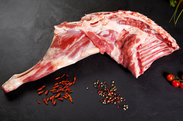 Fresh and raw meat. Leg of lamb uncooked tomato and pepper on black background - Photo, Image
