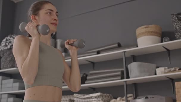 Döntse fel alacsony szögben lövés fiatal sportos nő csinál álló súlyzó sajtó gyakorlat edzés közben a tornaterem - Felvétel, videó
