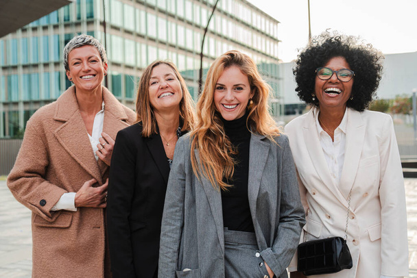 Egy csapat büszke üzletasszony mosolyog és kamerába néz a munkahelyén. Igazi vezető nők bámulnak elöl, együtt nevetnek öltönyben és sikeres kifejezéssel. Vállalati női munkavállalók ülése - Fotó, kép