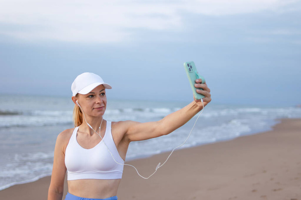 fille coureuse court le long de la plage en vêtements de sport. fille prend un selfie sur le bord de la mer avant le jogging. Photo de haute qualité - Photo, image