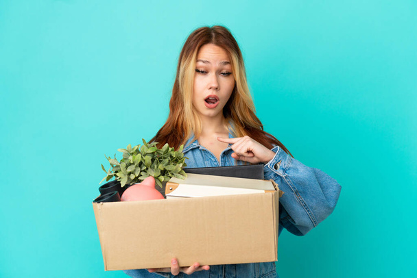 Chica rubia adolescente haciendo un movimiento mientras recoge una caja llena de cosas con expresión facial sorpresa - Foto, imagen
