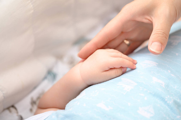 Pieni käsi vastasyntyneen vauvan lähikuva, äiti tukee vauvaa. - Valokuva, kuva