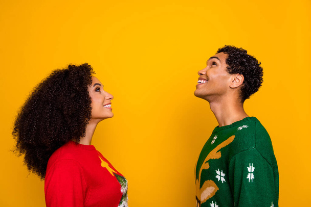 Photo of pretty dreamy guy girl dressed christmas ugly print pullovers looking up empty space isolated yellow color background. - 写真・画像