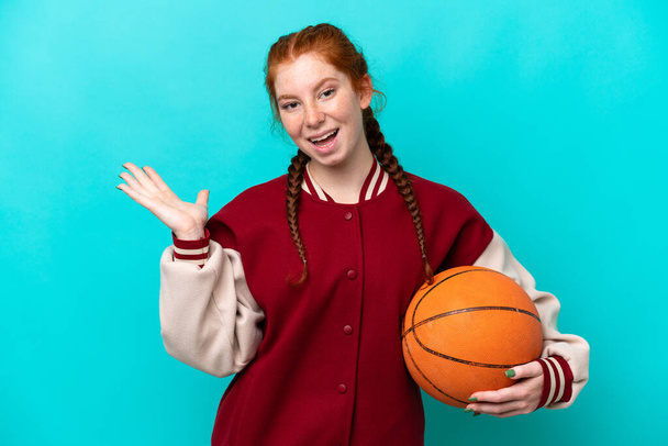 Молодая красноватая женщина играет в баскетбол на голубом фоне с шокированным выражением лица - Фото, изображение