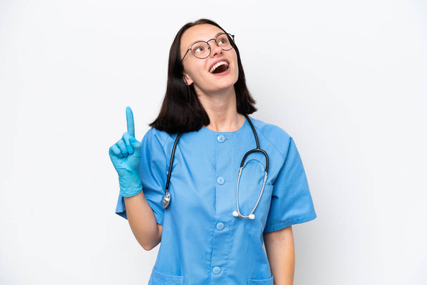 Nuori sairaanhoitaja valkoihoinen nainen eristetty valkoisella taustalla osoittaa ylös ja yllättynyt - Valokuva, kuva