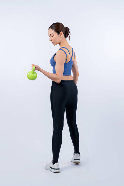 Vigorous energetic woman doing kettlebell weight lifting exercise on isolated background. Young athletic asian woman strength and endurance training session as body workout routine. - Photo, Image