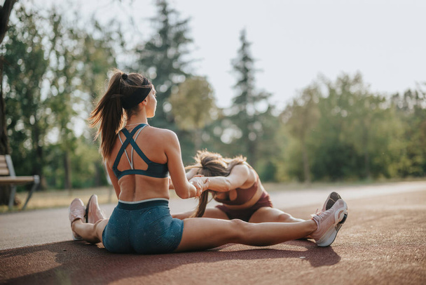 Fit girls inspireren een gezonde levensstijl buiten, stretchen en trainen in een groen park. Hun atletiek en motivatie zijn boeiend, het bevorderen van oefening doelen en uithoudingsvermogen. - Foto, afbeelding