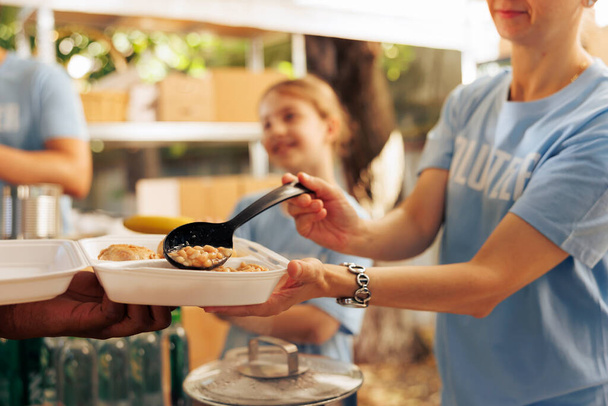 Een close-up shot van een blanke liefdadigheidswerker die verse warme maaltijden aanbiedt van een voedselbank in de buitenlucht tot een persoon in nood. Gedetailleerde weergave van gratis voedsel voor de hongerigen en minder bedeelden. - Foto, afbeelding