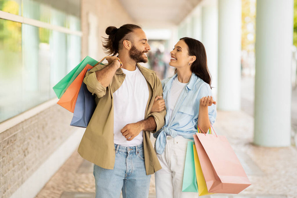 Ικανοποιημένοι χιλιετή καυκάσια κυρία και ο τύπος shopaholics με πολλά πακέτα, απολαμβάνουν ψώνια μαζί, νέα ρούχα χαμόγελο στο εμπορικό κέντρο. Περπατήστε, πώληση και σχέσεις, έκπτωση, διασκέδαση και αγάπη - Φωτογραφία, εικόνα
