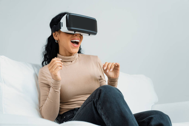 Νεαρή γυναίκα που χρησιμοποιεί εικονική πραγματικότητα VR goggle στο σπίτι για κρίσιμη εμπειρία online αγορών. Η καινοτομία εικονικής πραγματικότητας VR βελτιστοποιημένη για τον γυναικείο τρόπο ζωής ψηφιακής ψυχαγωγίας. - Φωτογραφία, εικόνα