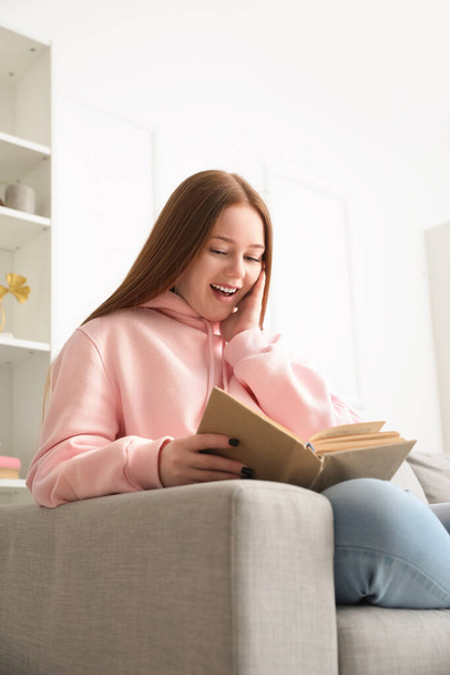 Onnellinen teini tyttö lukeminen kirja sohvalla kotona - Valokuva, kuva