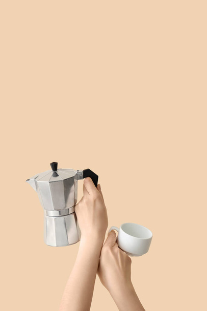 Женские руки держа чашку и гейзер кофеварка на бежевом фоне - Фото, изображение