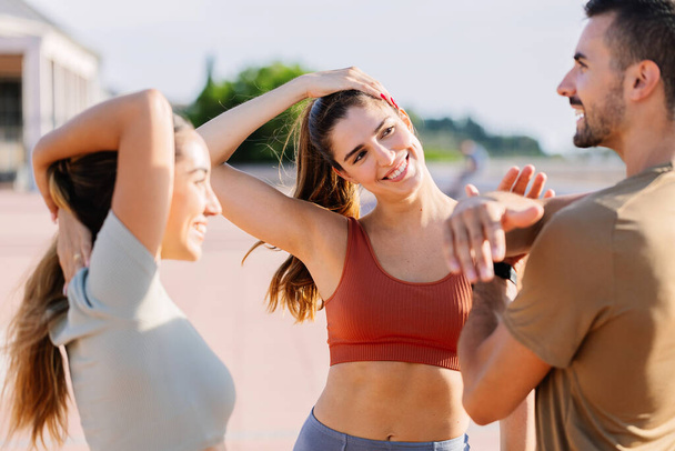 Drei junge Fitnessteams dehnen sich gemeinsam im Freien. Millennial fitte Menschen bereiten sich auf die Trainingsroutine auf der Straße vor - Foto, Bild