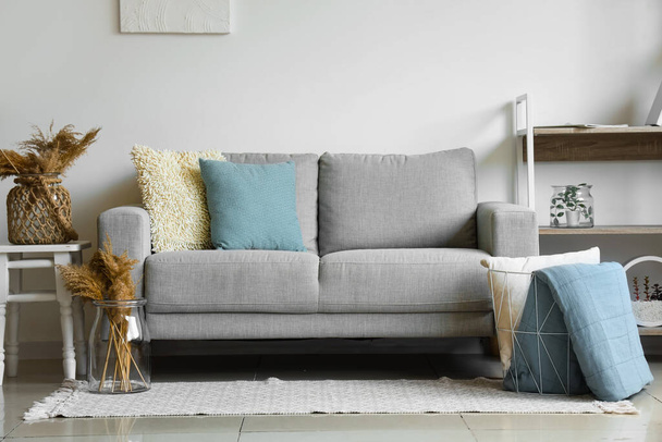 Útulná šedá pohovka a koš s měkkou přikrývkou v interiéru obývacího pokoje - Fotografie, Obrázek