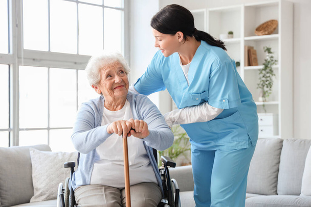 Mujer mayor en silla de ruedas con palo y enfermera en casa - Foto, Imagen