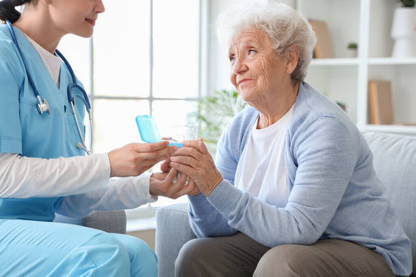 Starsza kobieta z pielęgniarką zażywającą tabletki w domu - Zdjęcie, obraz