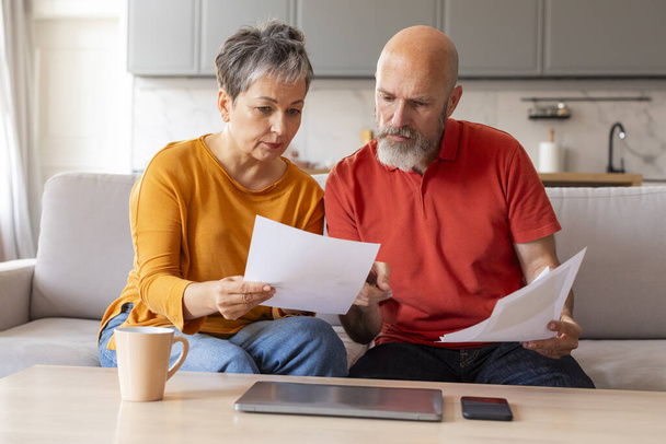 Stressed Senior Couple Checking Financial Papers And Planning Budget At Home, Upset Elderly Husband And Wife Looking At Loan Documents, Suffering Crisis While Calculating Family Spends, Closeup - 写真・画像