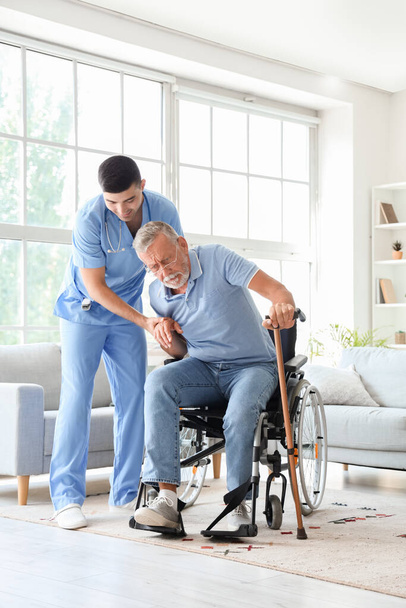 Мужчина-медсестра помогает старшему мужчине с палкой, чтобы встать дома - Фото, изображение