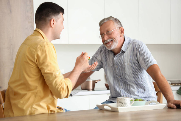 Молодой человек кормит отца на кухне - Фото, изображение