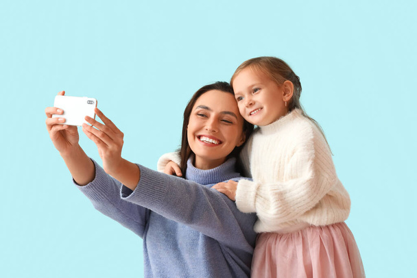 Η νεαρή μητέρα και η μικρή της κόρη βγάζουν selfie σε μπλε φόντο - Φωτογραφία, εικόνα
