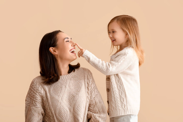 Kleine dochter aanraken neus van haar moeder op beige achtergrond - Foto, afbeelding