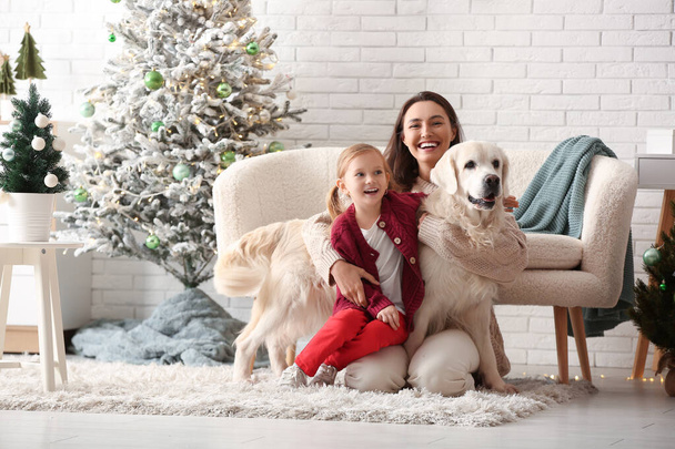 Счастливая молодая мать и ее маленькая дочь с милой собакой лабрадор у себя дома в канун Рождества - Фото, изображение