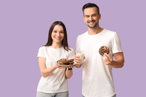 Jeune couple avec de savoureux biscuits et un verre de lait sur fond lilas - Photo, image