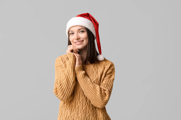 Όμορφη νεαρή γυναίκα με το καπέλο Santa σε γκρίζο φόντο - Φωτογραφία, εικόνα