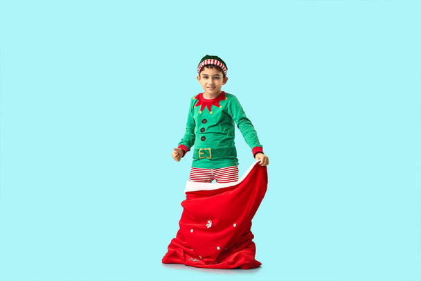 Lindo pequeño elfo con bolsa de Santa mostrando el pulgar hacia arriba sobre fondo azul - Foto, imagen